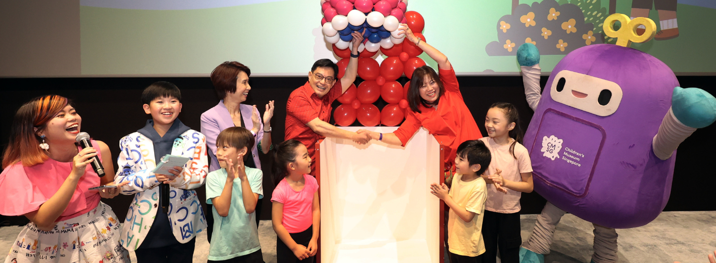 People and a mascot at Children’s Museum Singapore, shaking hands over balloons for an event.